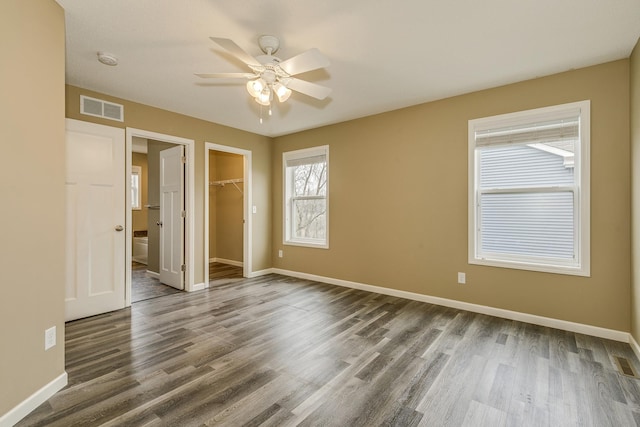 unfurnished bedroom with baseboards, a walk in closet, dark wood-type flooring, and visible vents