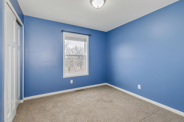 carpeted spare room featuring baseboards, a textured ceiling, and visible vents