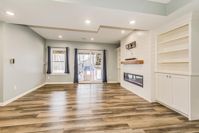 unfurnished living room with dark wood-style flooring, a large fireplace, built in features, baseboards, and recessed lighting