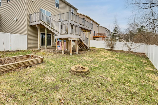 rear view of house featuring a deck, a fenced backyard, a lawn, an outdoor fire pit, and stairway