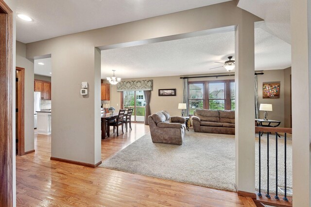 living room featuring recessed lighting, baseboards, light wood-style flooring, and ceiling fan with notable chandelier