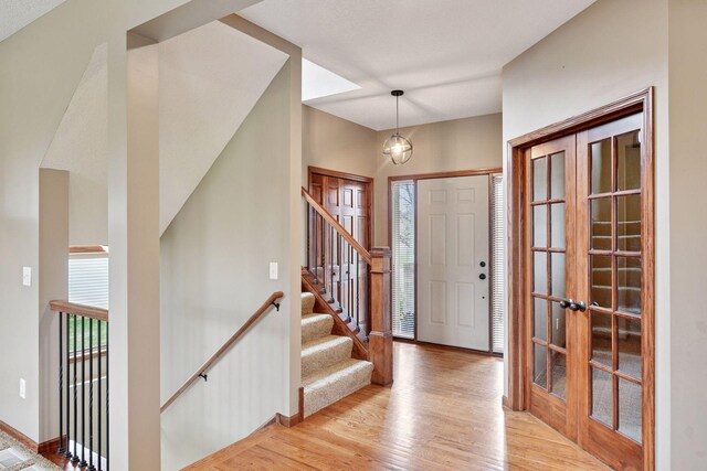foyer featuring light wood-style floors, baseboards, french doors, and stairway