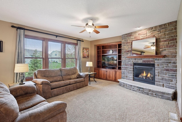 carpeted living room with built in shelves, ceiling fan, a textured ceiling, and a stone fireplace