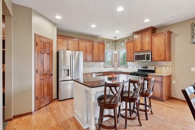 kitchen with appliances with stainless steel finishes, brown cabinetry, a sink, and light wood finished floors