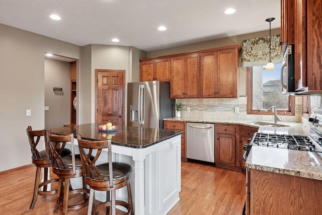 kitchen with brown cabinetry, a breakfast bar, a sink, light wood-style flooring, and appliances with stainless steel finishes