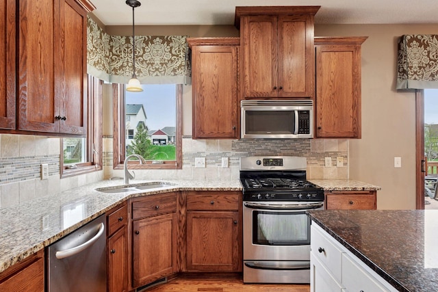 kitchen with brown cabinets, stainless steel appliances, a sink, and dark stone counters