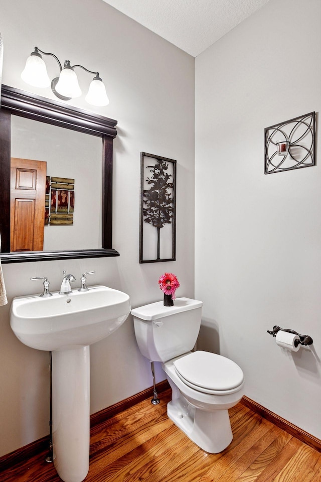 half bath featuring a sink, baseboards, toilet, and wood finished floors