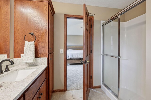 ensuite bathroom featuring tile patterned floors, a shower stall, baseboards, and vanity