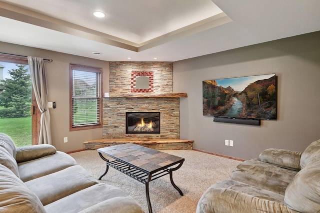 carpeted living room with baseboards, a tray ceiling, recessed lighting, and a stone fireplace