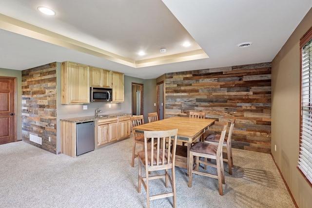kitchen featuring light brown cabinets, stainless steel microwave, light colored carpet, and dishwasher