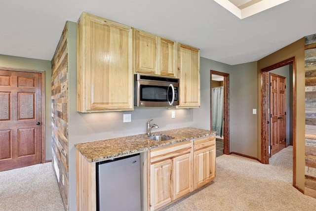 kitchen with a sink, light brown cabinets, light carpet, and stainless steel appliances