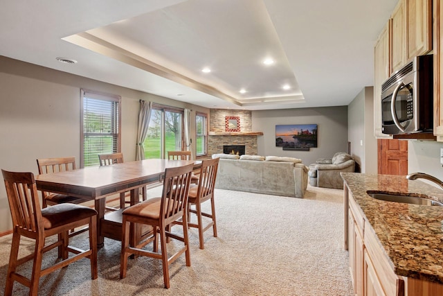 dining room featuring recessed lighting, a raised ceiling, light carpet, and a fireplace