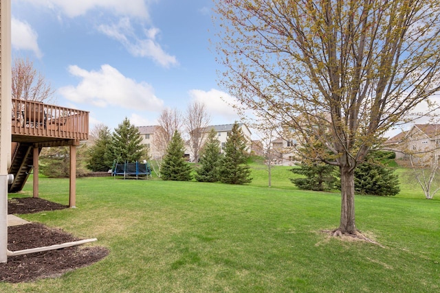 view of yard featuring a deck, stairs, and a trampoline