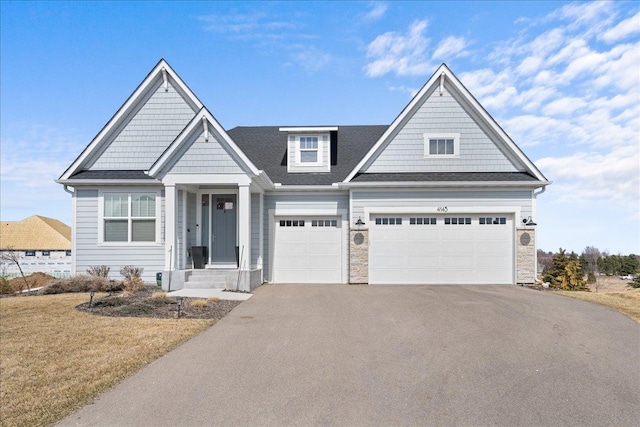 craftsman house featuring a shingled roof, stone siding, a front yard, and aphalt driveway
