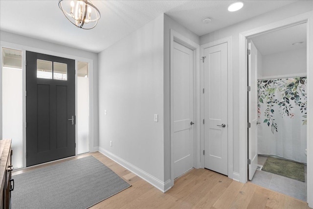 foyer with baseboards, light wood-type flooring, and a notable chandelier