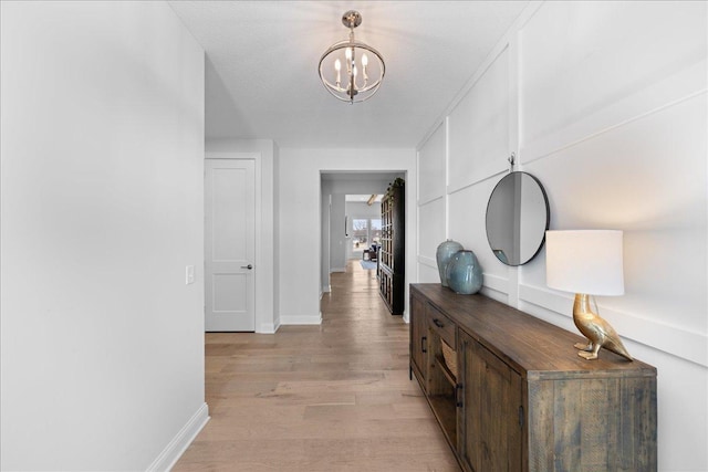 hallway with an inviting chandelier, baseboards, and light wood finished floors
