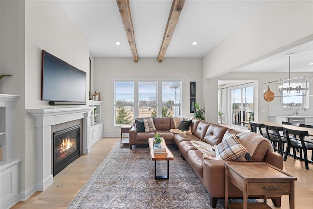 living area featuring a glass covered fireplace, recessed lighting, beamed ceiling, and light wood finished floors
