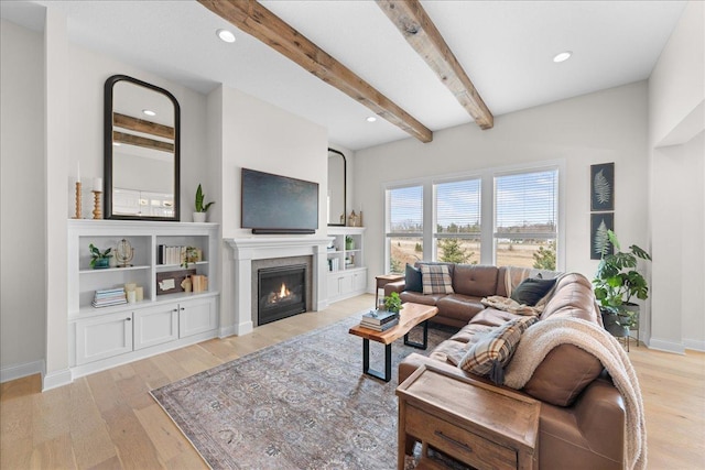 living room with a glass covered fireplace, baseboards, light wood-type flooring, and beam ceiling