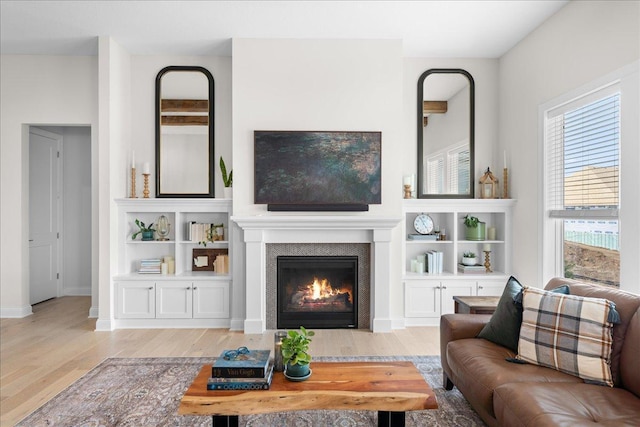 living area featuring a glass covered fireplace, baseboards, and wood finished floors