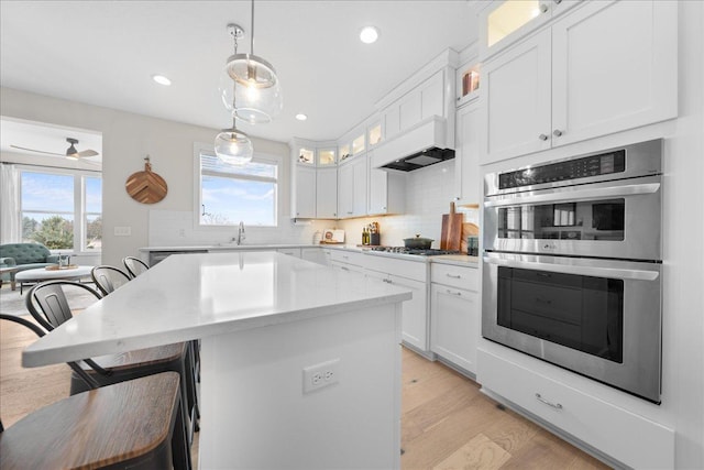 kitchen with a breakfast bar, a center island, stainless steel double oven, tasteful backsplash, and light wood finished floors