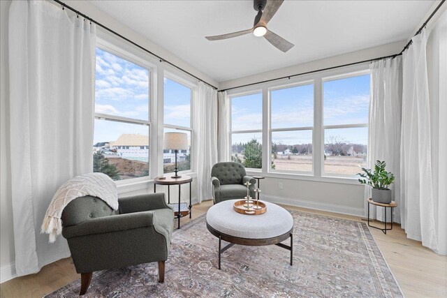 living area featuring a ceiling fan, baseboards, and light wood-style floors
