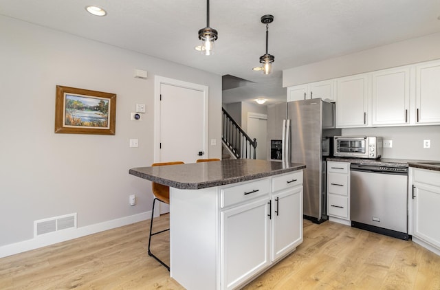 kitchen with appliances with stainless steel finishes, dark countertops, light wood finished floors, a center island, and white cabinetry