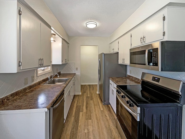 kitchen featuring decorative backsplash, dark countertops, a sink, light wood finished floors, and appliances with stainless steel finishes