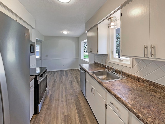 kitchen with dark wood-style flooring, dark countertops, tasteful backsplash, a sink, and appliances with stainless steel finishes