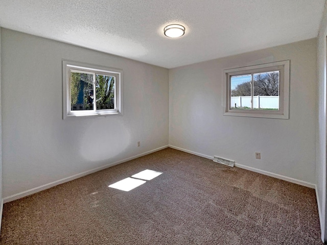 carpeted empty room with a textured ceiling, baseboards, and visible vents