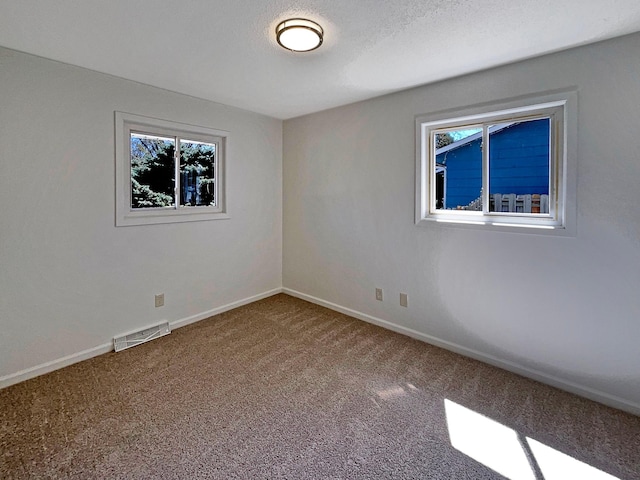 carpeted empty room featuring baseboards, visible vents, and plenty of natural light