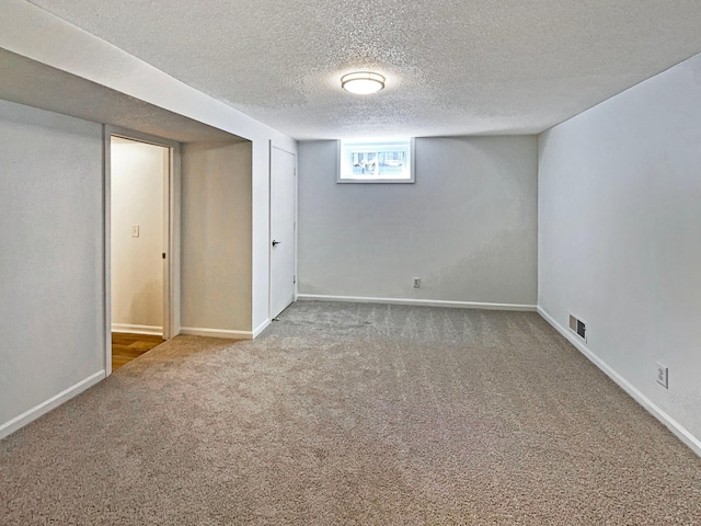 below grade area with a textured ceiling, baseboards, visible vents, and carpet
