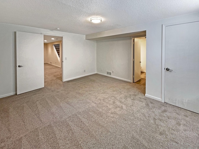 finished basement with carpet flooring, a textured ceiling, stairs, baseboards, and visible vents