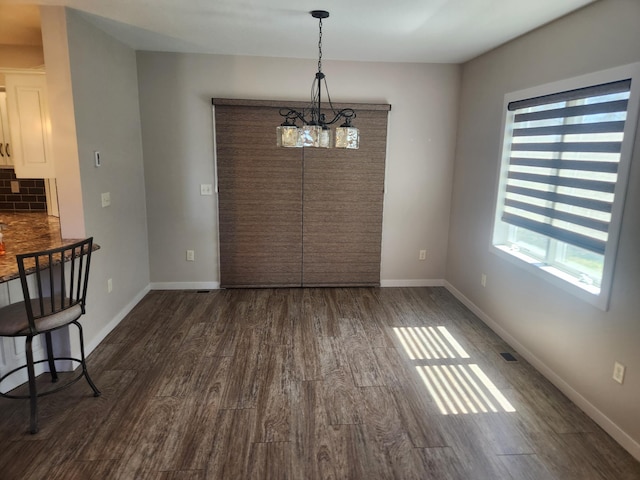 unfurnished dining area featuring an inviting chandelier, baseboards, and dark wood-style flooring