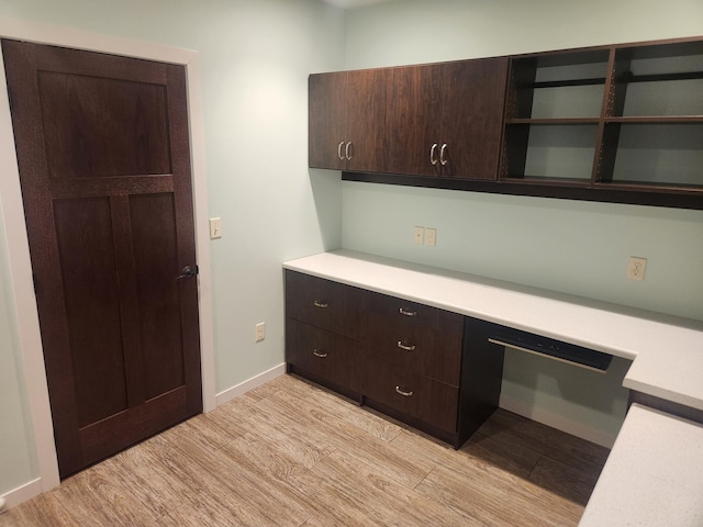 kitchen with dark brown cabinetry, open shelves, light wood finished floors, light countertops, and baseboards