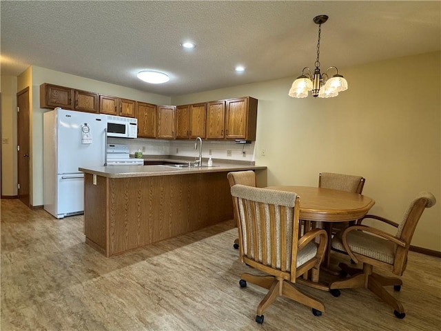 kitchen featuring brown cabinets, a sink, white appliances, a peninsula, and decorative light fixtures