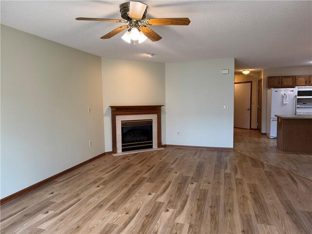 unfurnished living room featuring a ceiling fan, baseboards, a glass covered fireplace, and light wood-style floors
