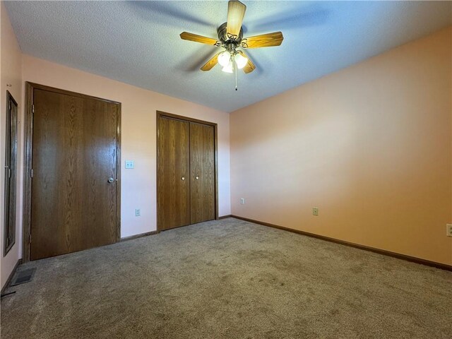 unfurnished bedroom with ceiling fan, a textured ceiling, baseboards, two closets, and carpet