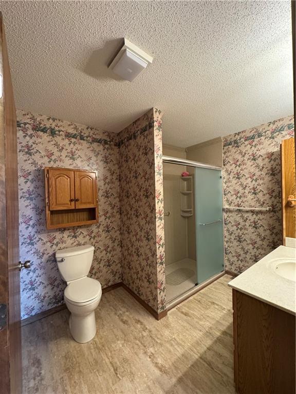 full bath featuring a textured ceiling, a shower stall, wood finished floors, vanity, and toilet
