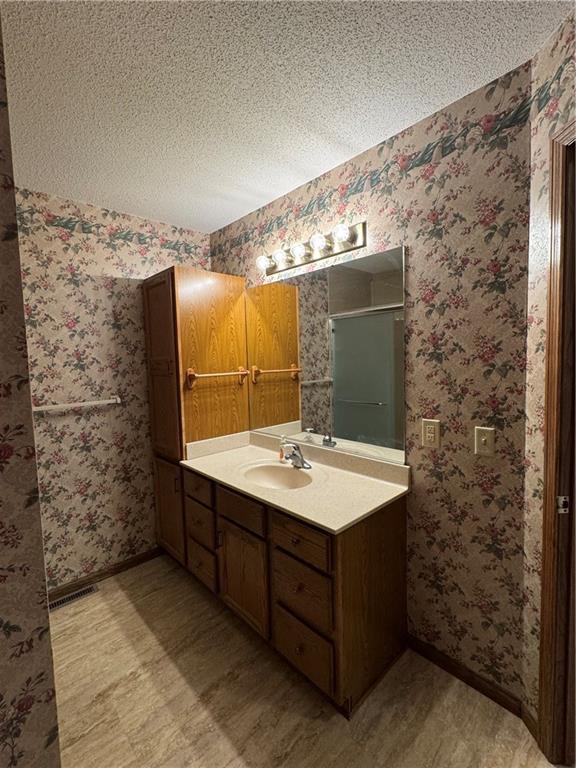 full bathroom with vanity, a textured ceiling, baseboards, and a shower stall