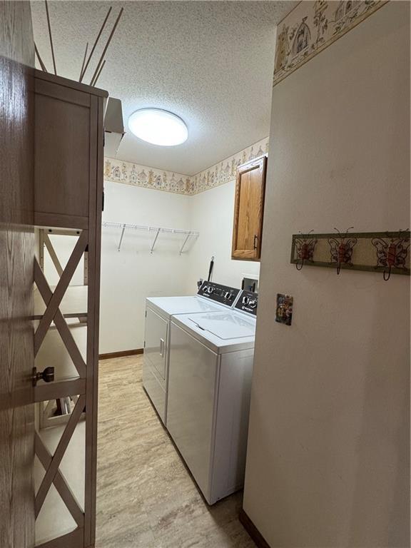 clothes washing area featuring a textured ceiling, baseboards, cabinet space, and washing machine and clothes dryer