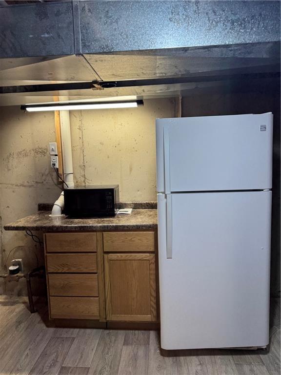 kitchen featuring black microwave, dark countertops, freestanding refrigerator, and light wood-type flooring