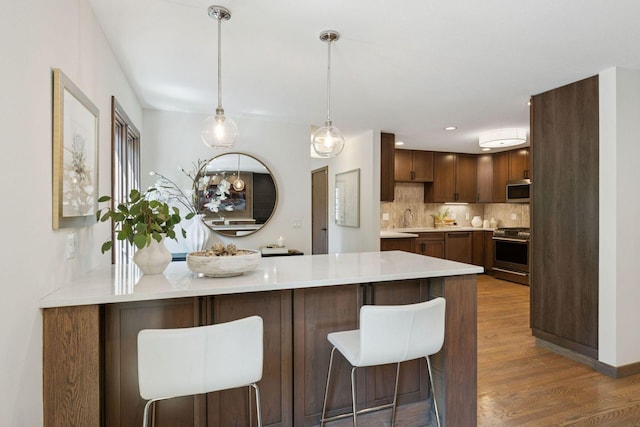 7000 Lanham Ln, Edina, MN 55439 - kitchen featuring stainless steel appliances, a peninsula, wood finished floors, a breakfast bar, and decorative backsplash