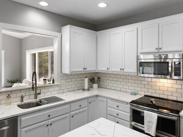 kitchen featuring white cabinetry, light stone counters, a sink, appliances with stainless steel finishes, and backsplash