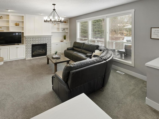 carpeted living room featuring baseboards, a notable chandelier, visible vents, and a tile fireplace