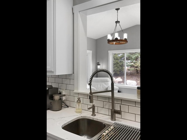 kitchen featuring decorative backsplash, a sink, light stone counters, white cabinets, and lofted ceiling
