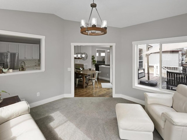 living room featuring an inviting chandelier, baseboards, vaulted ceiling, and dark colored carpet