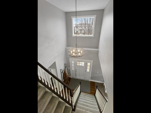 foyer with baseboards, stairway, a textured ceiling, a chandelier, and carpet flooring