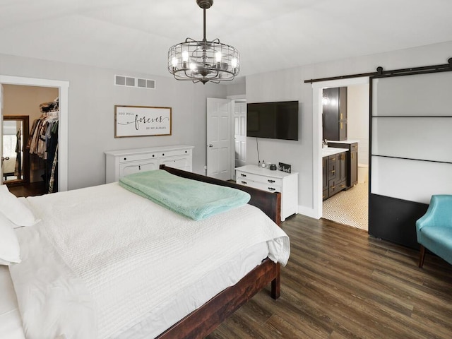 bedroom with a notable chandelier, a barn door, a walk in closet, wood finished floors, and visible vents