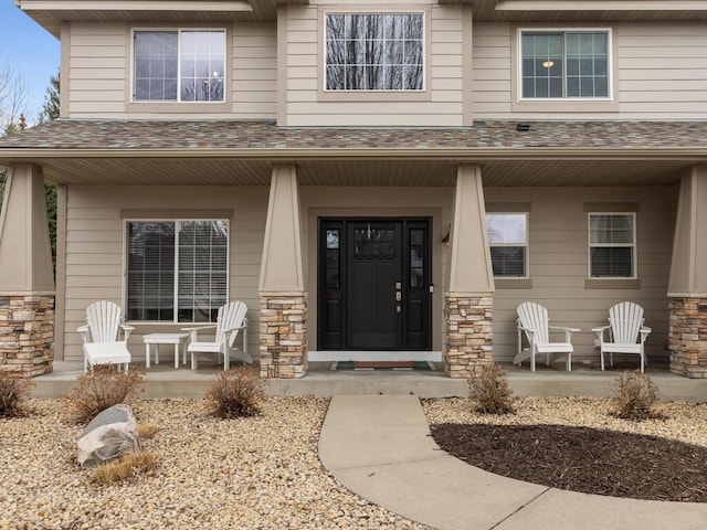 entrance to property with covered porch, a shingled roof, and stone siding