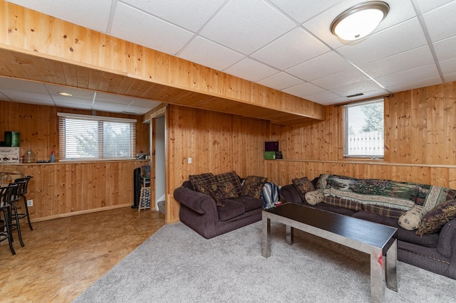 living room with baseboards, a drop ceiling, and wooden walls